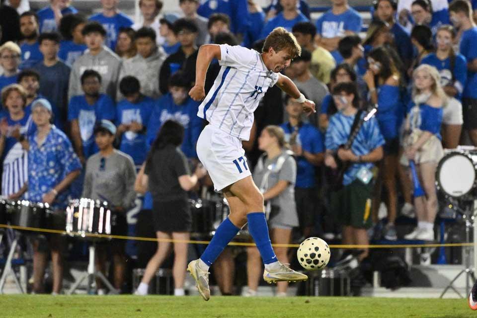Male soccer player jumps up to make contact with the ball during a night game.