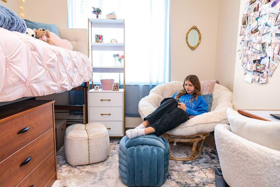 A female student is seated in a lounge chair on their phone.