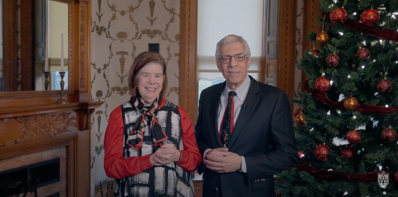 Screenshot from Christmas video of the Pestellos standing in front of a Christmas tree and fireplace and smiling.