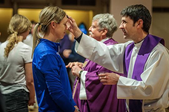Priest applies the cross of ashes to girl on Ash Wednesday
