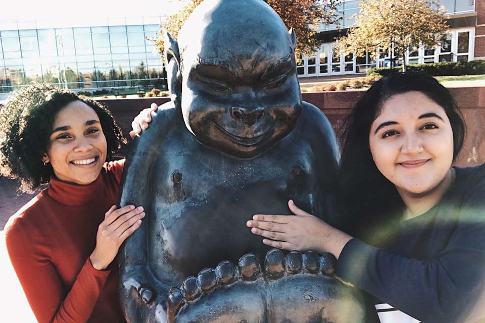 Two students standing at Billiken statue