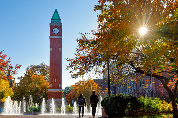 Two students walking next to SLU's clock tower on a spring day