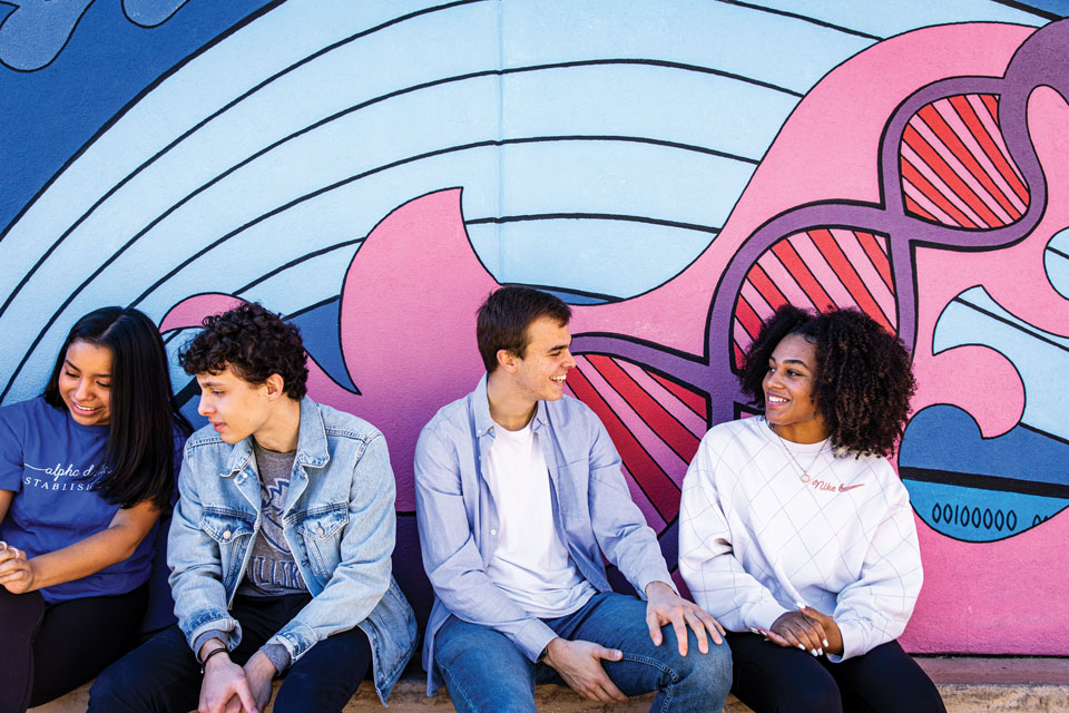 Four students talking in front of a painted mural. 
