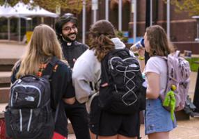 Students with backpacks in discussion with youthful campus priest