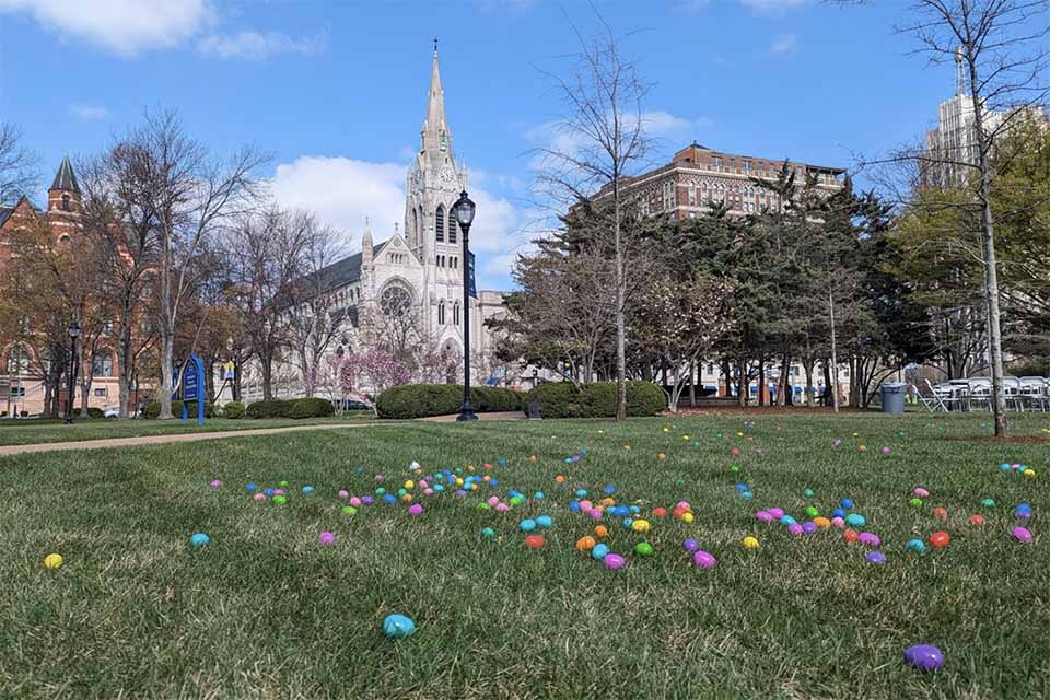 Colorful Easter eggs lay in the grass on SLU's campus with college church in the background