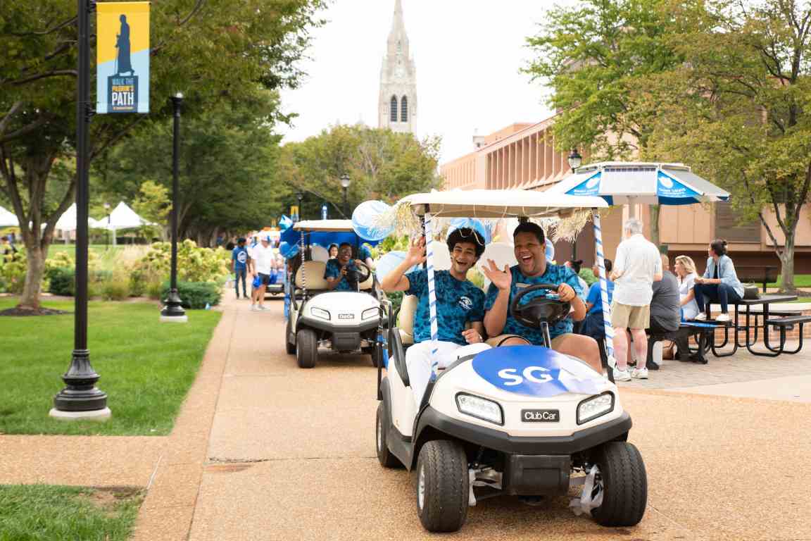 The Student Government Association golf cart drives across campus with College Church in the background