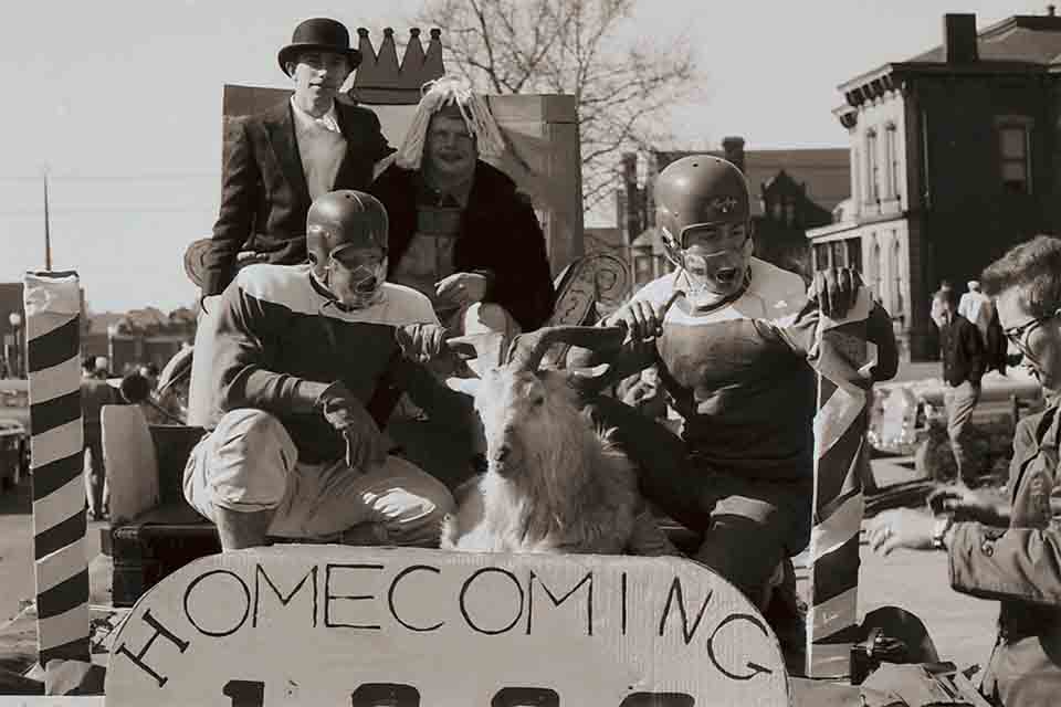 A group of SLU students in football uniforms pose with a goat on a parade float