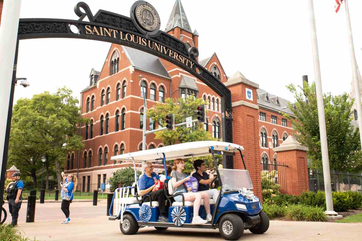 Dr Fred Pestello rides a golf cart through SLU's archways along Grand Boulevard in the 2023 golf cart parade