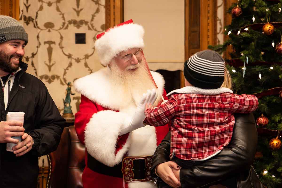 Santa Claus gives a child a high five with an adult smiling in the background