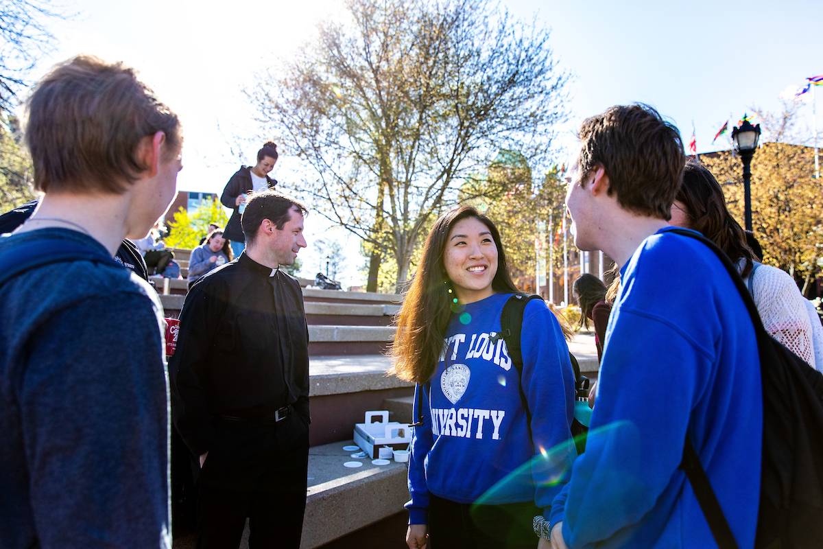 One of SLU's Jesuit faculty talks with a group of SLU students near the clock tower on the north campus.