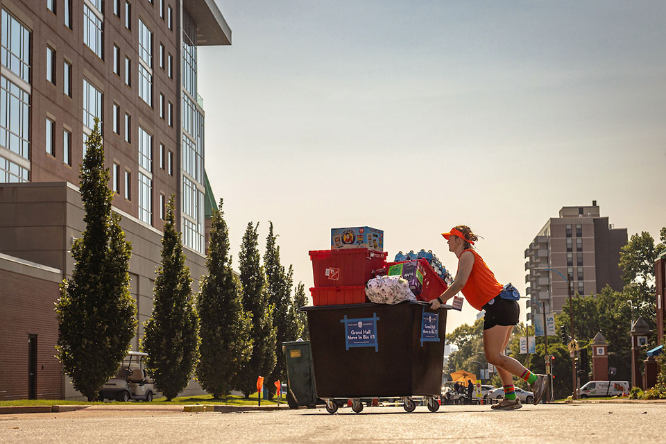 Oriflamme A student pushes a large bin filled with boxes across the street on campus.