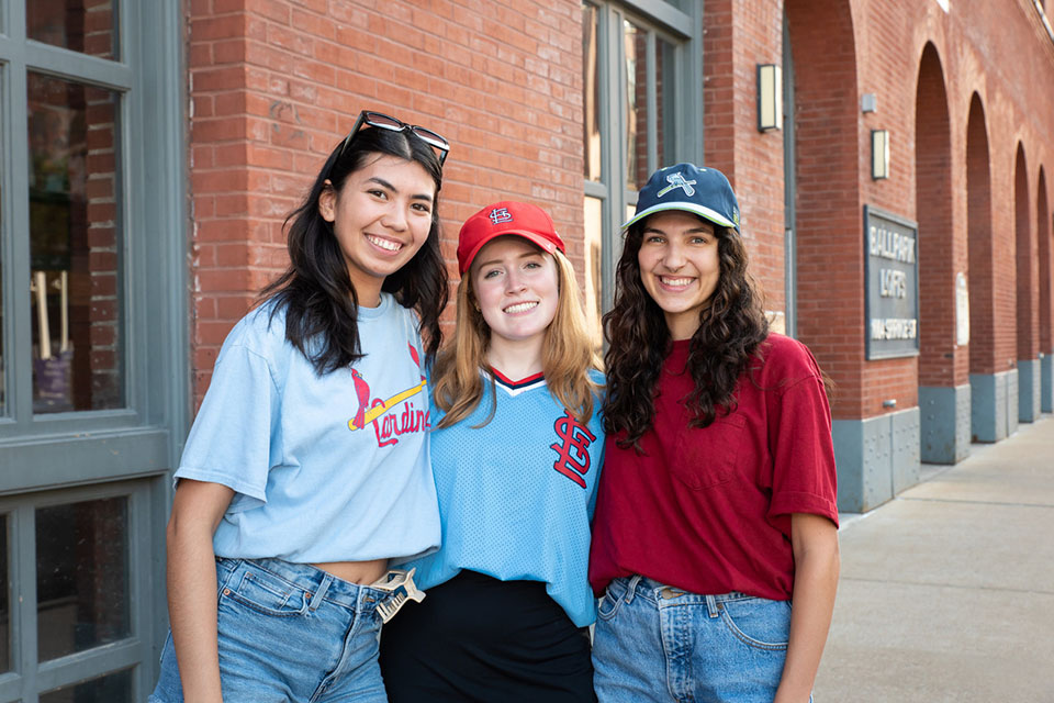 Three students pose for a photo wearing Cardinals merchandise.