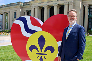Jody Sowell stands in front of a large heart decorated with the St. Louis City flag in front of the Missouri History Museum.