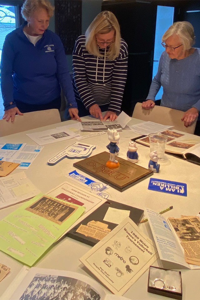 Volleyball alums Three women gather around a table looking at SLU volleyball memorbilia.