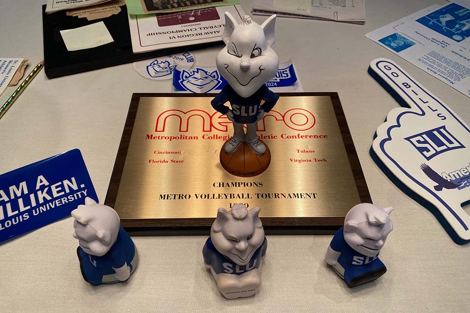 Volleyball Championship Title A plaque, small Billiken figurine and other SLU memorabilia sits on a table.