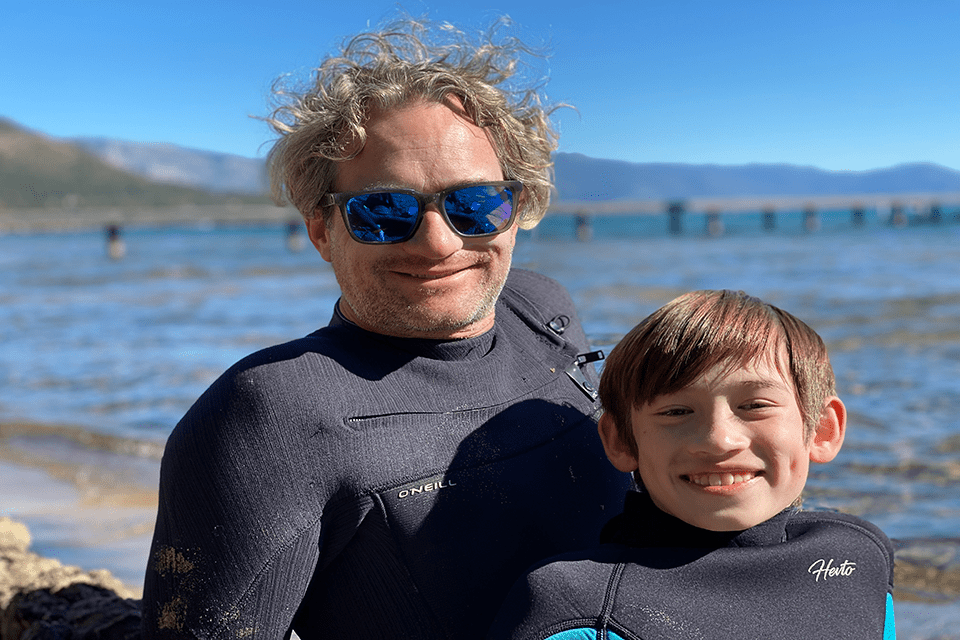 Travis Hoffstetter (A&S ‘05), and his son in wetsuits on a beach.