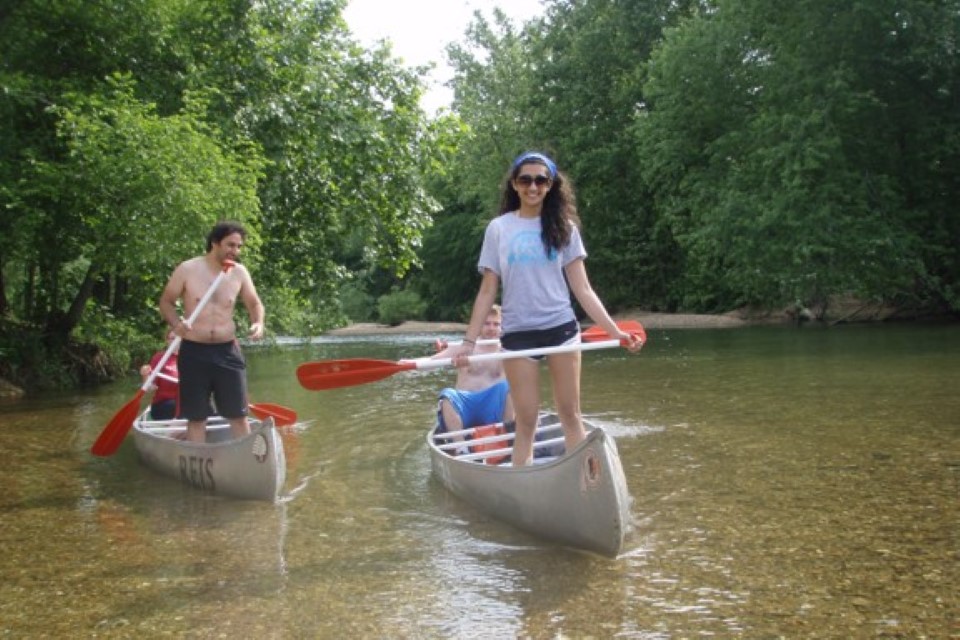 Students in canoes on a river with clear water and a rocky bottom.