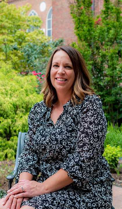 A portrait of Keli Jackson sitting outside with trees and a red brick building in the background