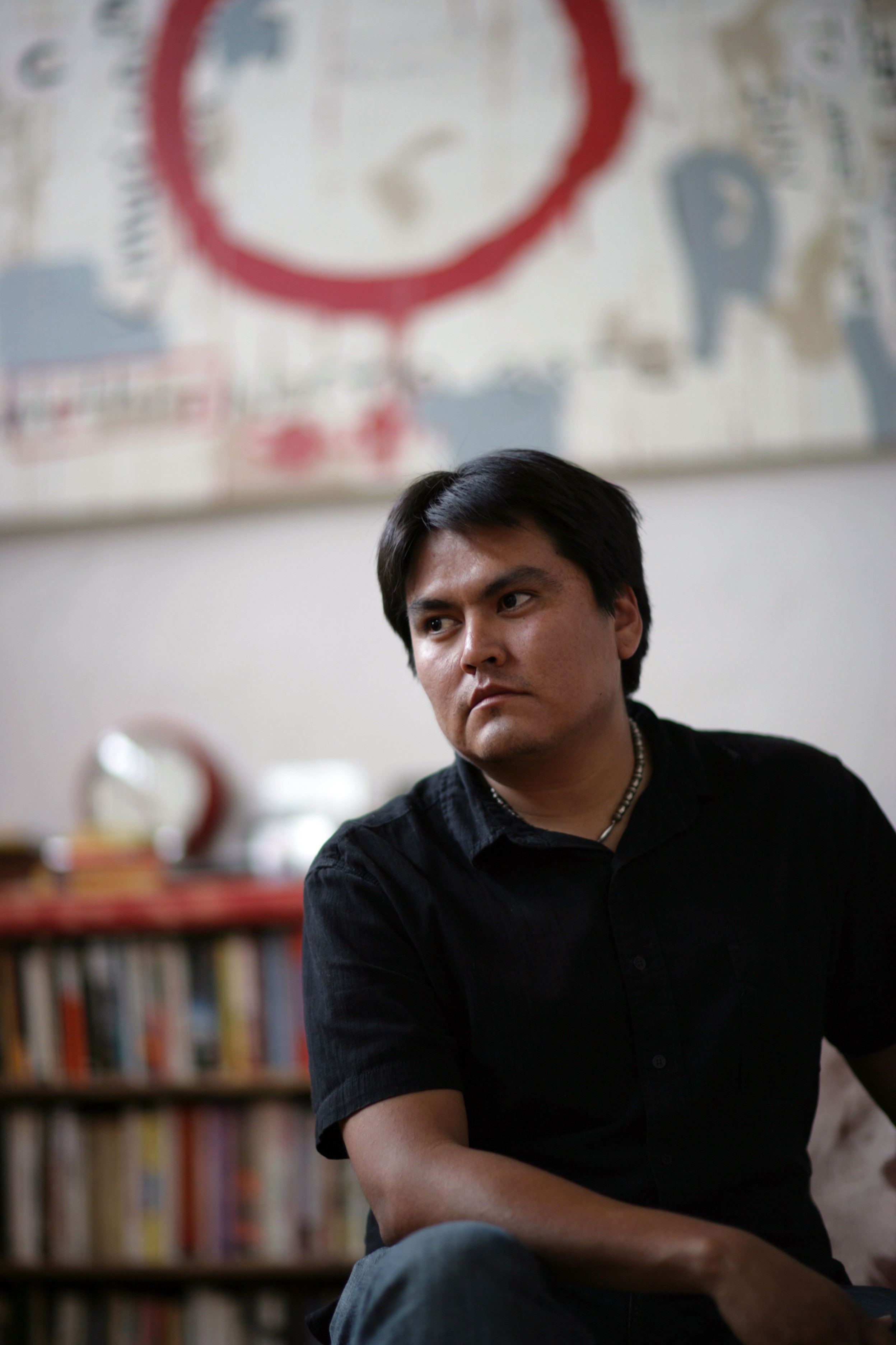 Sherwin Bitsui sitting in front of book shelves.