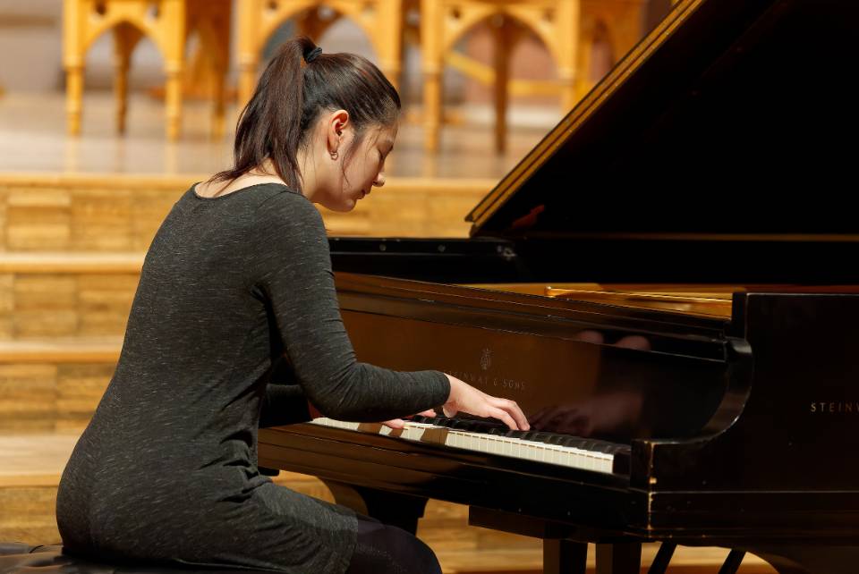 A student plays a grand piano during a concert.