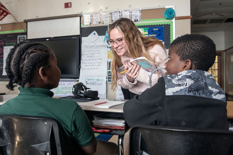 Student teacher interacting with two elementary students in a classroom 