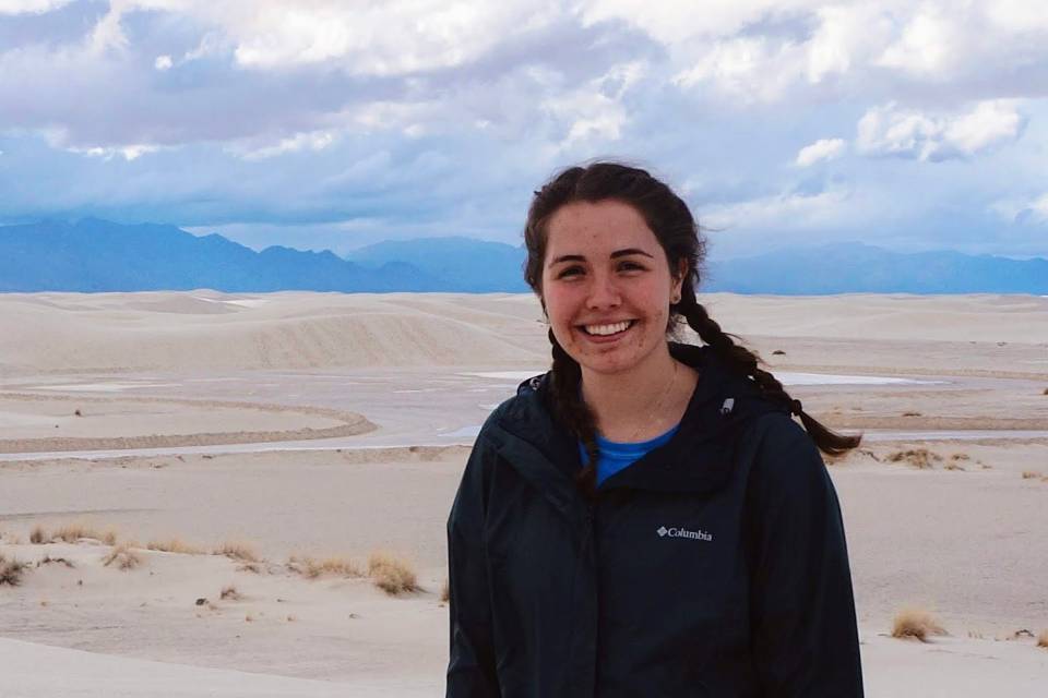 Lilly Williams stands in a landscape of sandy desert with mountains in the background