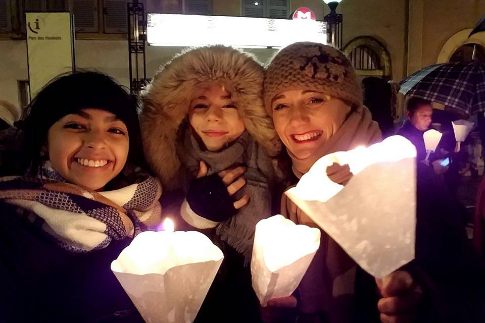 Student with host family members, wearing winter gear, at an outdoor festival, holding candles with paper holders.