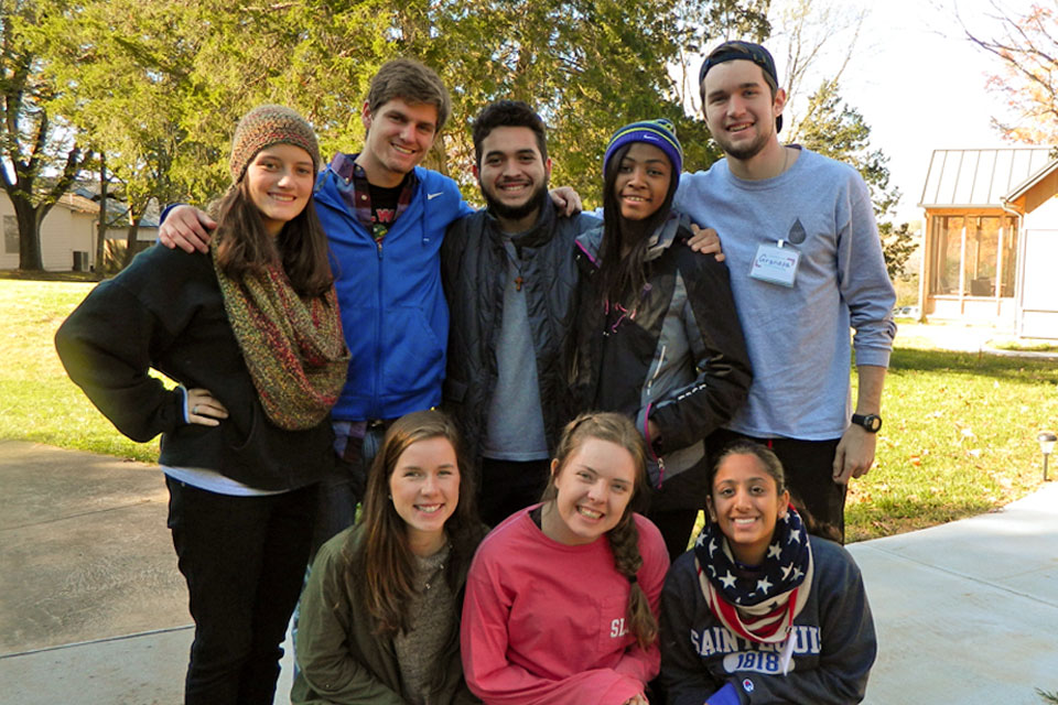 A group of 8 students pose for a photo outdoors while preparing for a retreat.