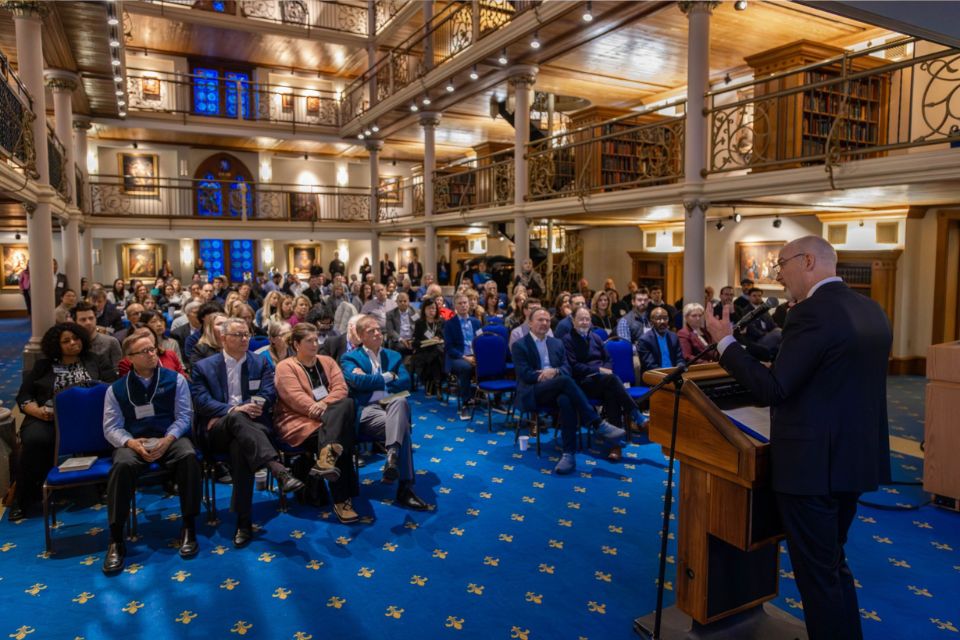 a man stands speaking at a podium speaking in front of a crowd of people