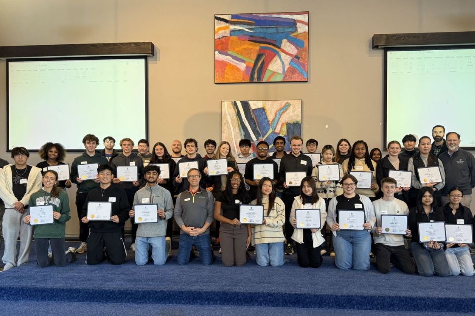 large group of people posing and holding certificate in front of projector screens