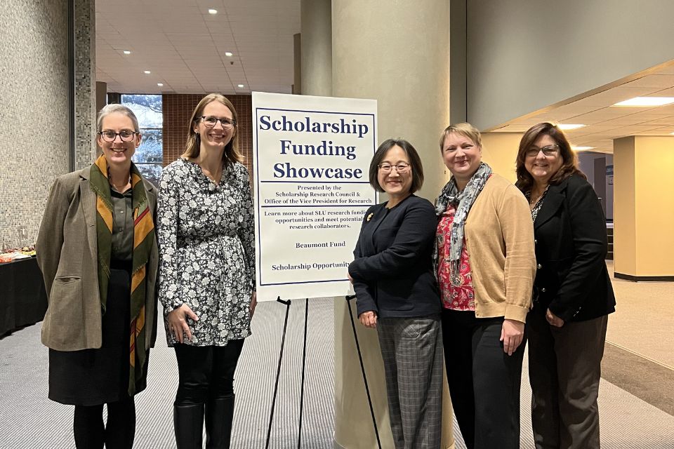 five women standing smiling and posed with a sign reading scholarship funding showcase sign