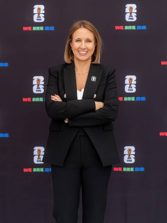 Amy Hopfinger wearing a business suit poses in front of a banner with the logo for the 2026 Fifa World Cup