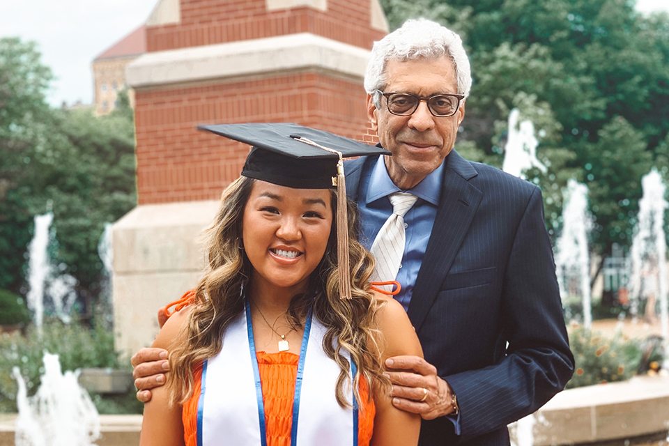 Cassidy Manns, One-Year MBA gradaute, poses for photo in her graduation cap in front of the Clock Tower fountains with Saint Louis University President Fred Pestello, Ph.D.