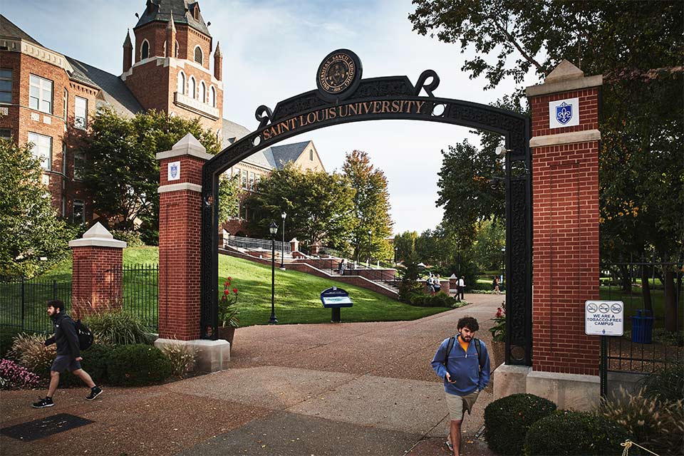A photo of the SLU gate way by Cook Hall with a student walking through