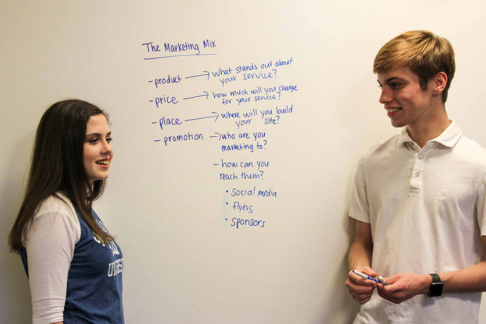 Chaifetz School students write business strategies on a whiteboard while serving as mentors during college access program hosted by St. Louis Internship Program at the Chaifetz School of Business.