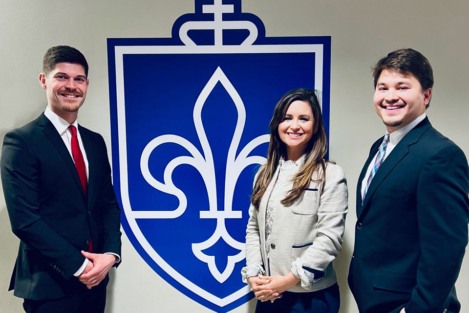 Constantin Heider, Lindsey Teague and Rio Pimentel pose for a photo in front of the Chaifetz School shield