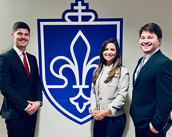 Saint Louis University students Rio Pimentel, Lindsey Teague and Constantin Heider pose for a photo in front of the Chaifetz School shield