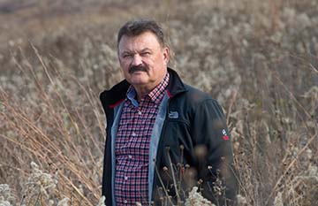 Rudi Roeslein looks at the camera while standing in a field of waist-high grasses.