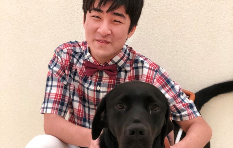 Seyoon Choi, an undergraduate student researcher in SLU's CHROME Lab, smiles while holding his service dog.