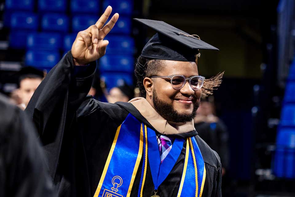A graduate in a cap, gown and stole waves to a crowd at SLU midyear 22 commencement