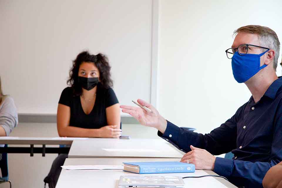 Two students in masks sitting at a classroom table