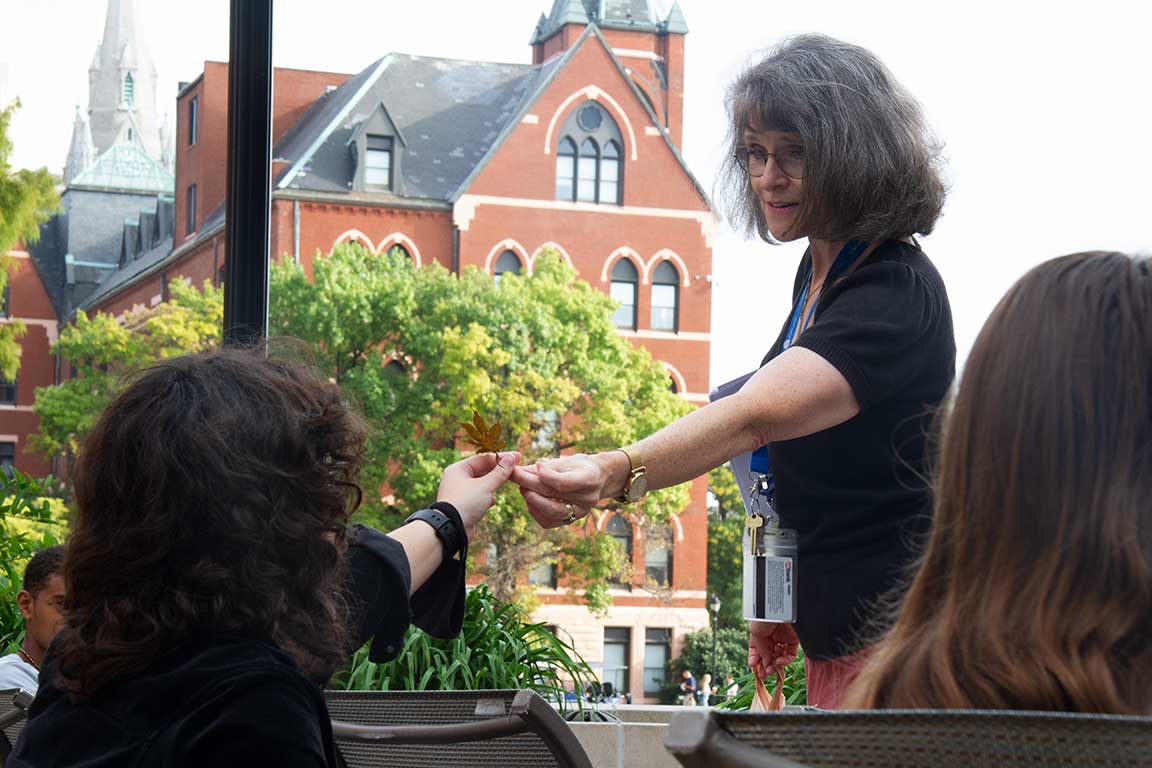 A professor stands over a seated student and hands her a leaf.