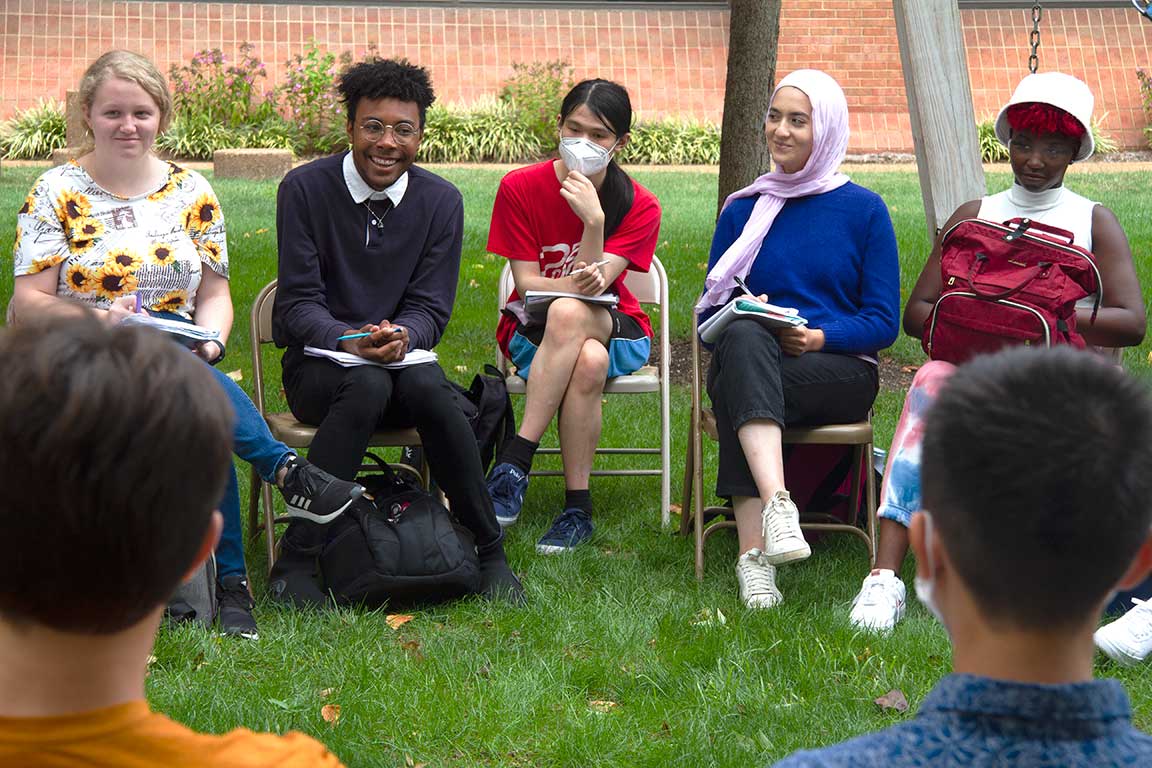 Students sit in on folding chairs in a semi circle outdoors during a discussion about social justice