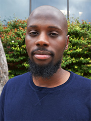 African American man in a navy blue shirts, facing the camera with a serious expression