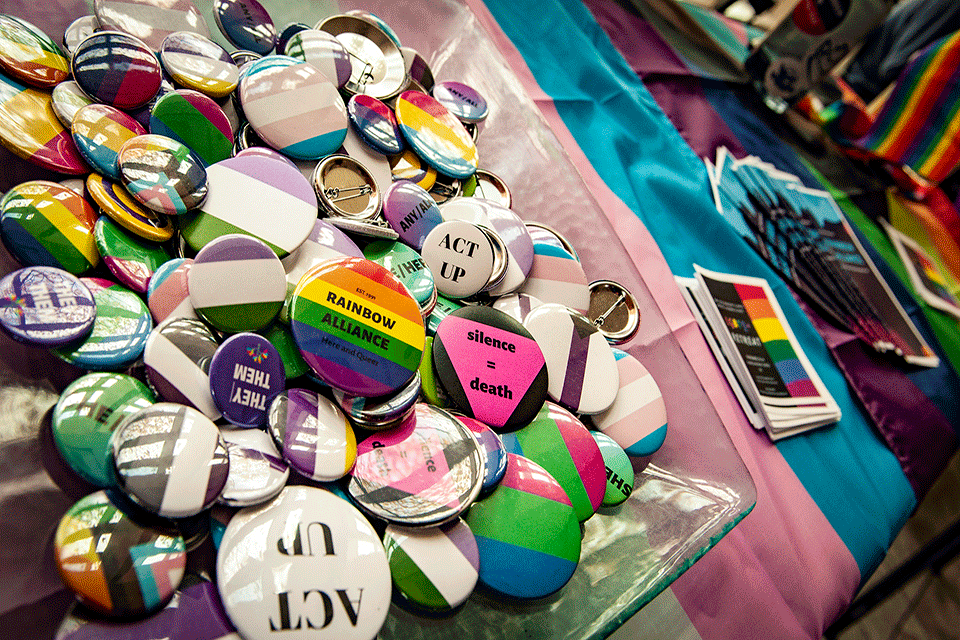 LGBT pins and buttons spread out on a table covered with a flag
