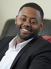 African American man smiling at the camera, wearing a white shirt and dark blazer