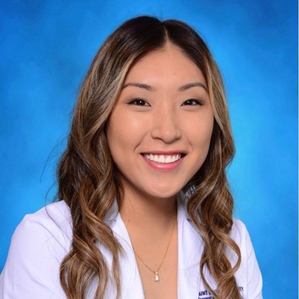 Jemma Kim wearing a white lab coat sitting in front of a blue background