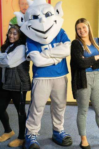 Two School of Education students and SLU Billiken mascot smiling with arms folded