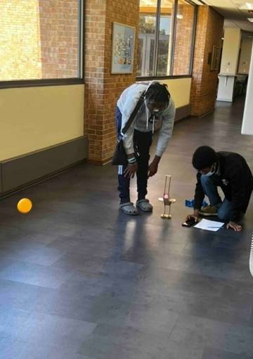 Two students are in a hallway, bending over their iSCORE launcher