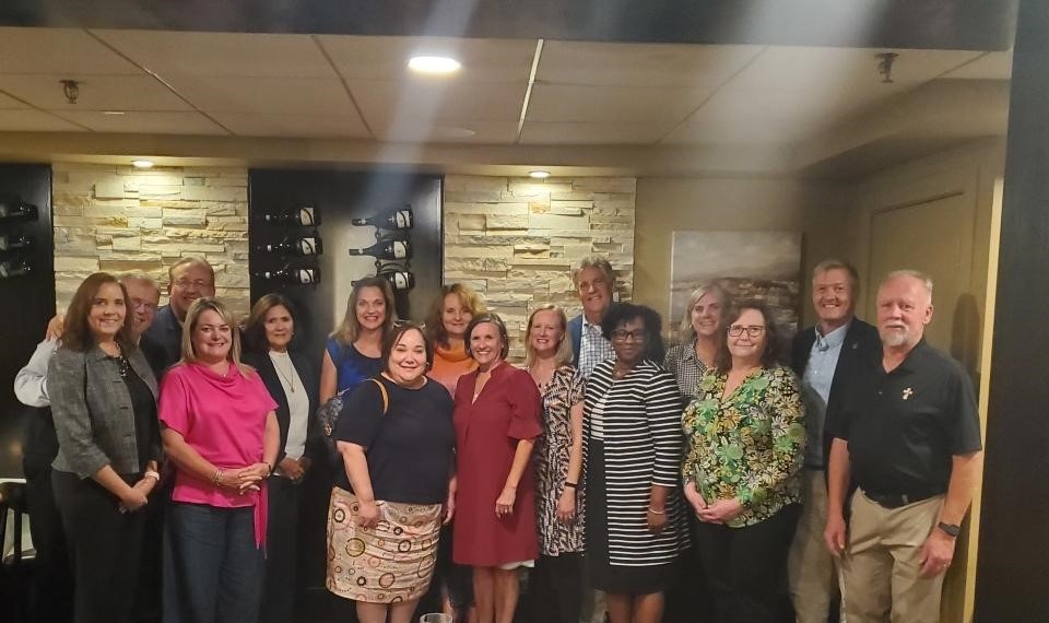 Program attendees pose and smile in front of a brick wall with a wine cellar.